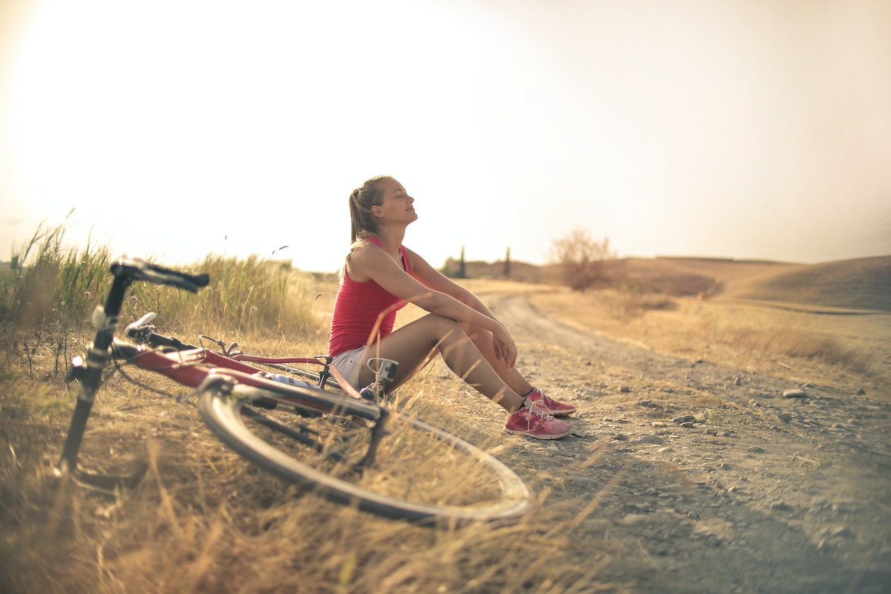 a happy woman sitting on the ground by a bike, finding a path to inner healing