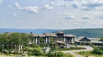Exterior view of Cloudland at McLemore Resort showing the main lodge building with stone and wood architecture nestled among trees on Lookout Mountain, with rolling green hills visible in the background.