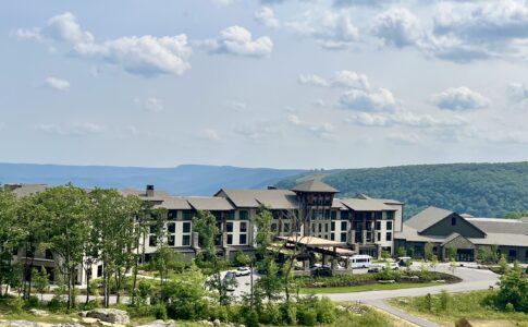 Exterior view of Cloudland at McLemore Resort showing the main lodge building with stone and wood architecture nestled among trees on Lookout Mountain, with rolling green hills visible in the background.