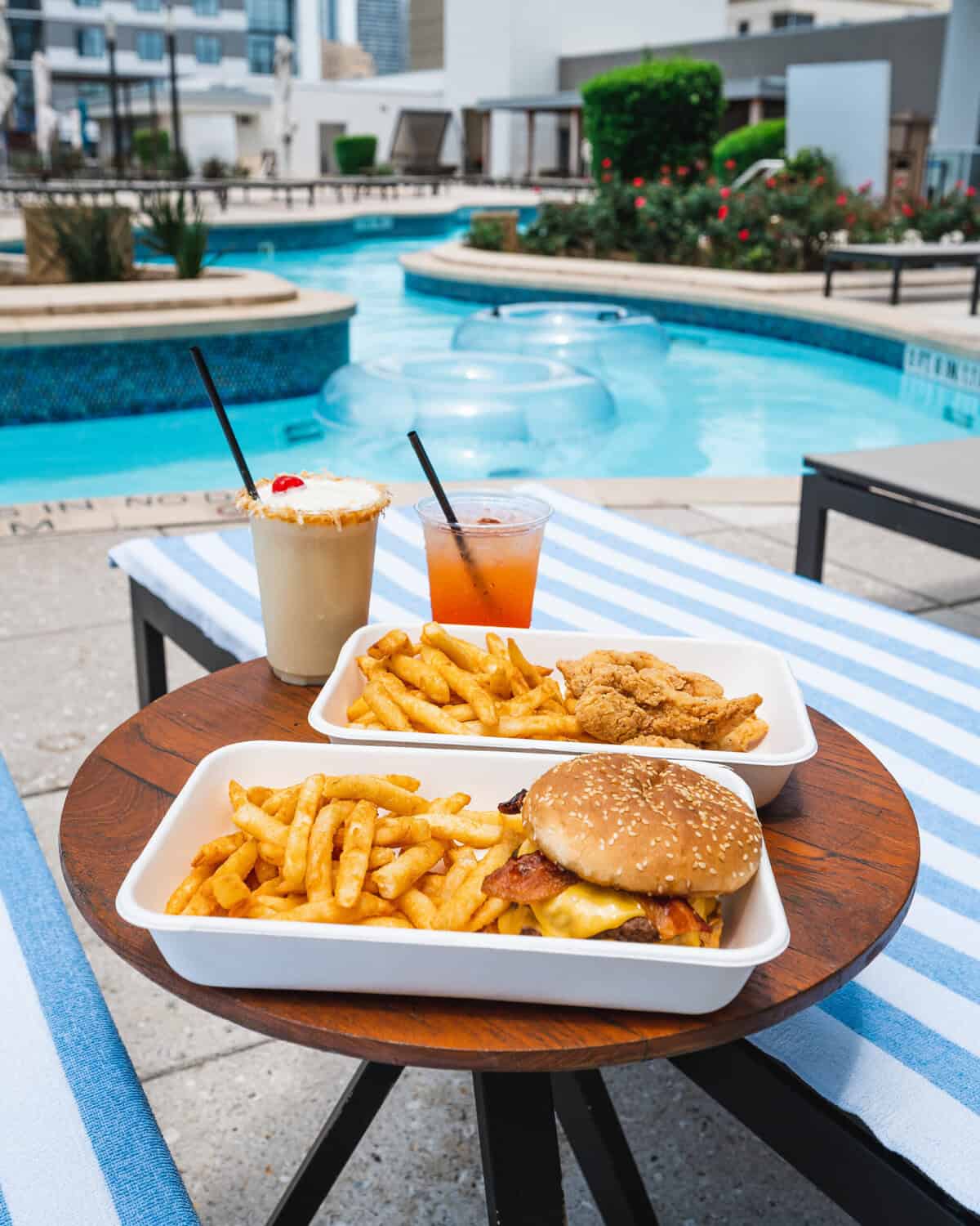 A burger and fries with drinks by a pool