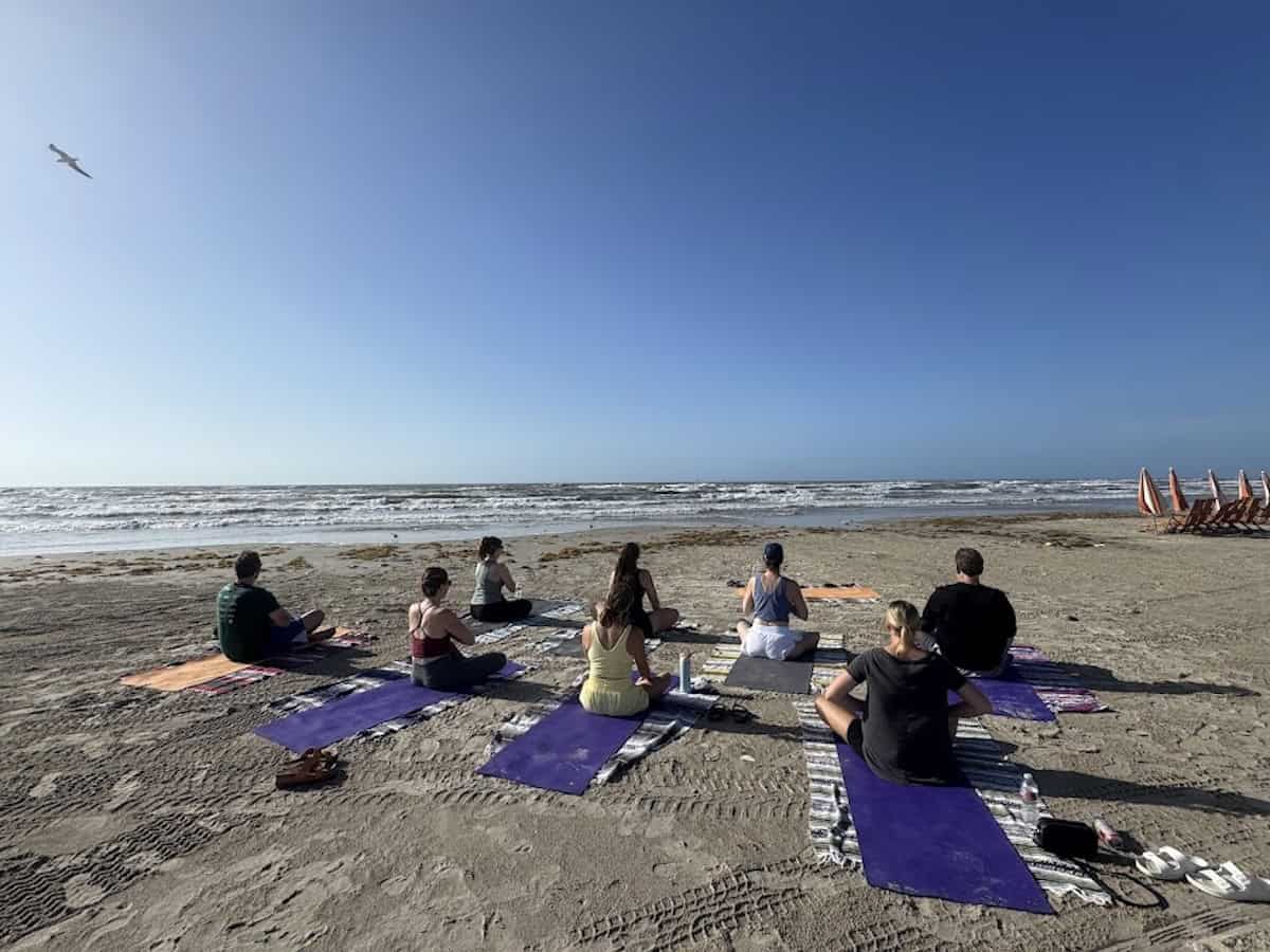People sitting on yoga mats on the beach.