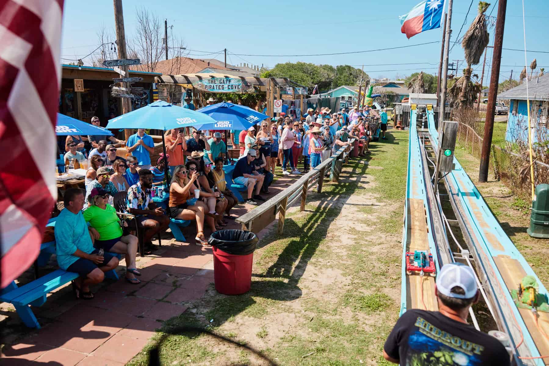 Two participants racing belt sanders on a long straightaway course as a crowd watches.