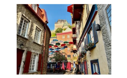 Colorful umbrellas hang above Rue du Petit-Champlain with Château Frontenac rising in the background.