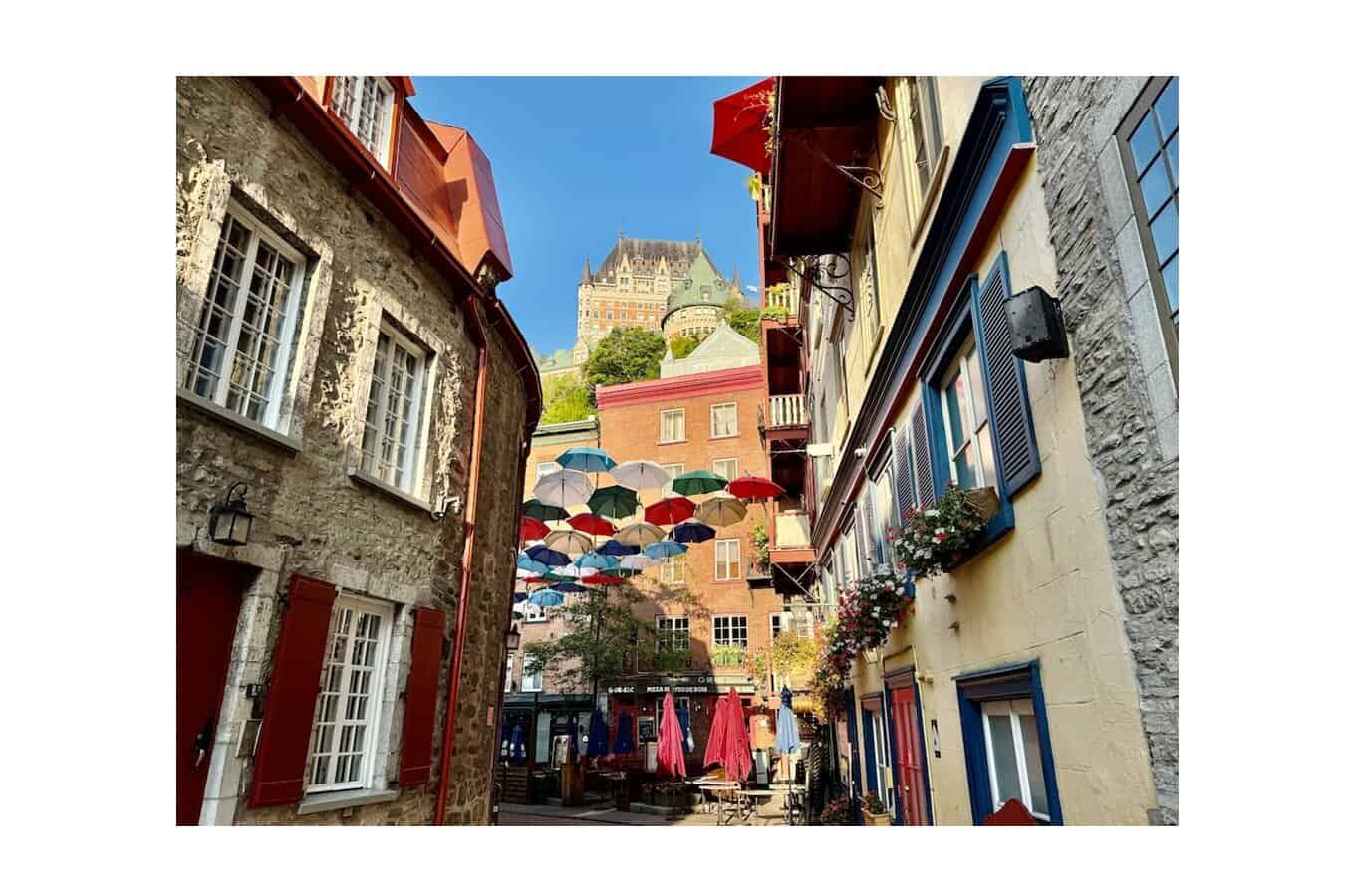 Colorful umbrellas hang above Rue du Petit-Champlain with Château Frontenac rising in the background.