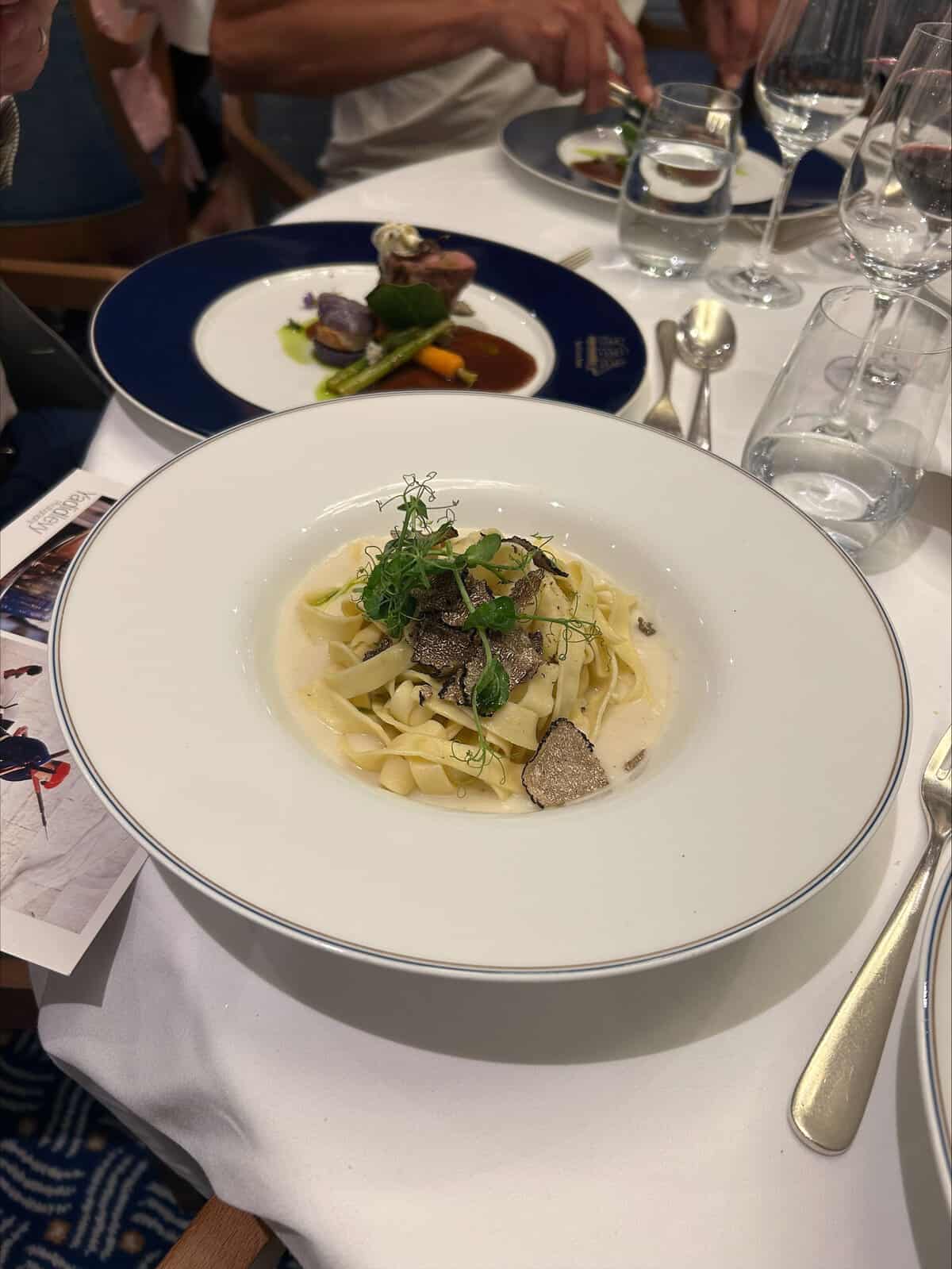 A plate of fresh pasta topped with shaved truffles and herbs on elegant white china.