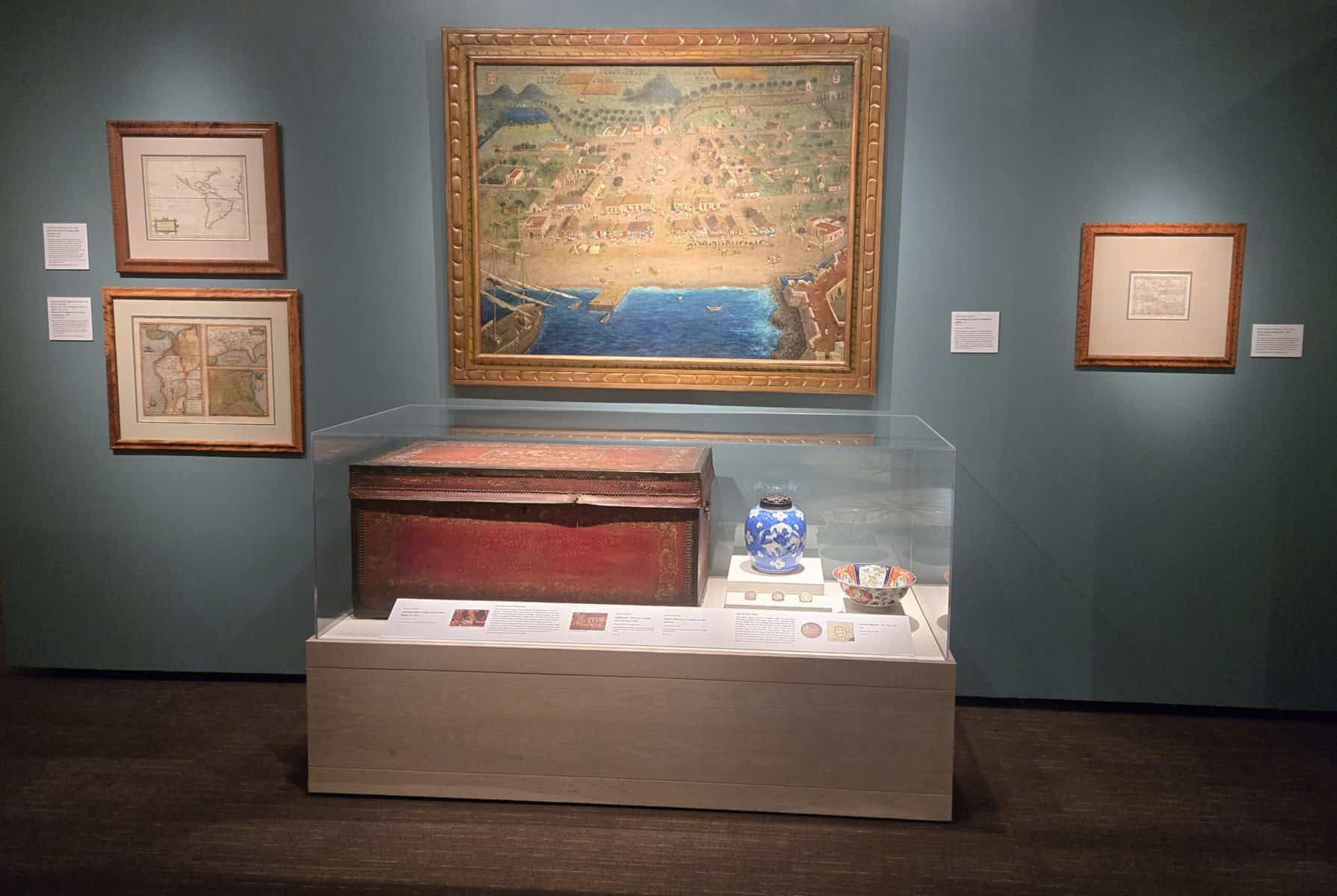Exhibition gallery showing framed Texas maps alongside display cases of period artifacts, with interpretive labels and warm gallery lighting.