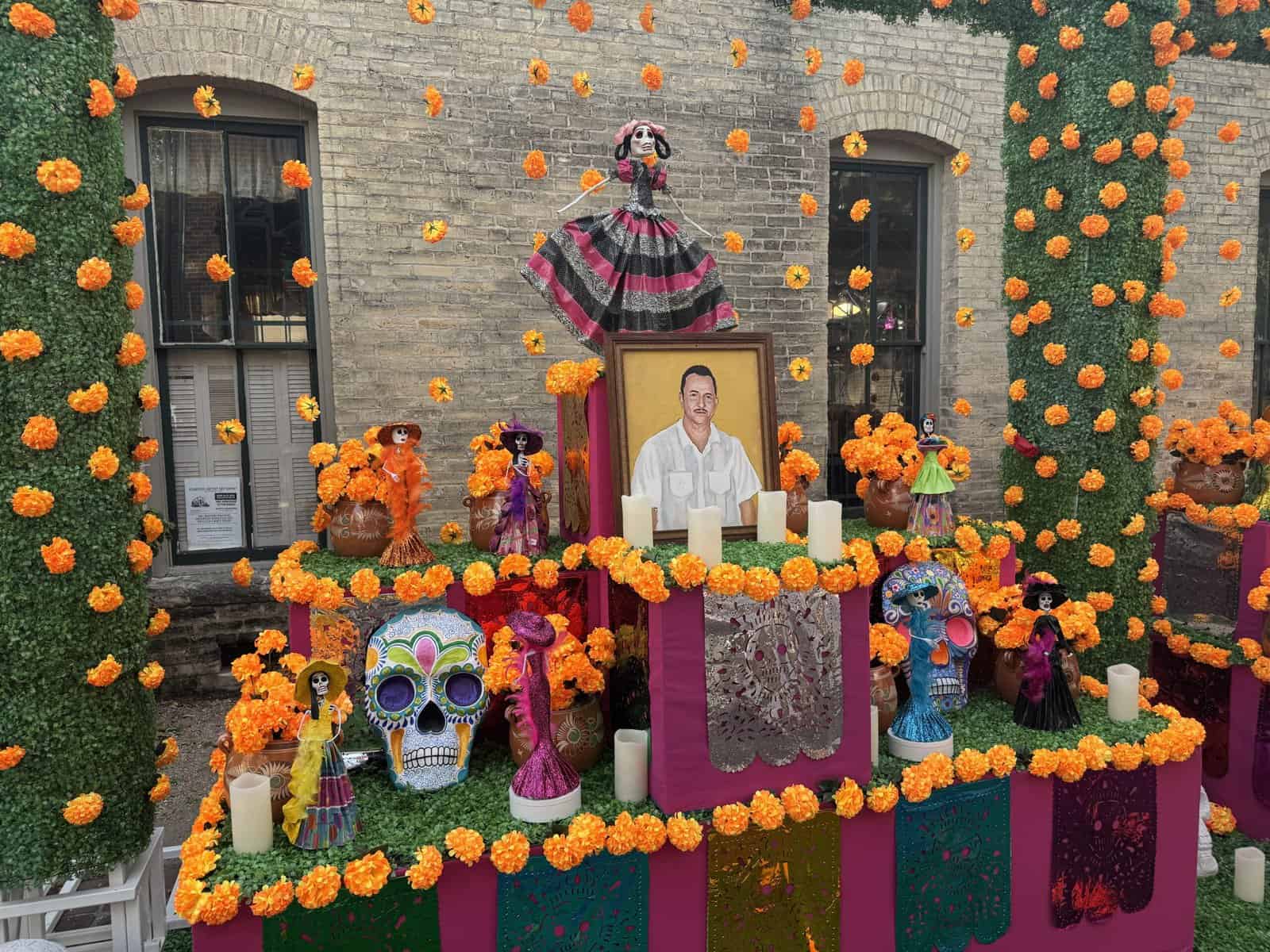 A Day of the Dead altar featuring a portrait, dancing catrinas, and marigold flowers.