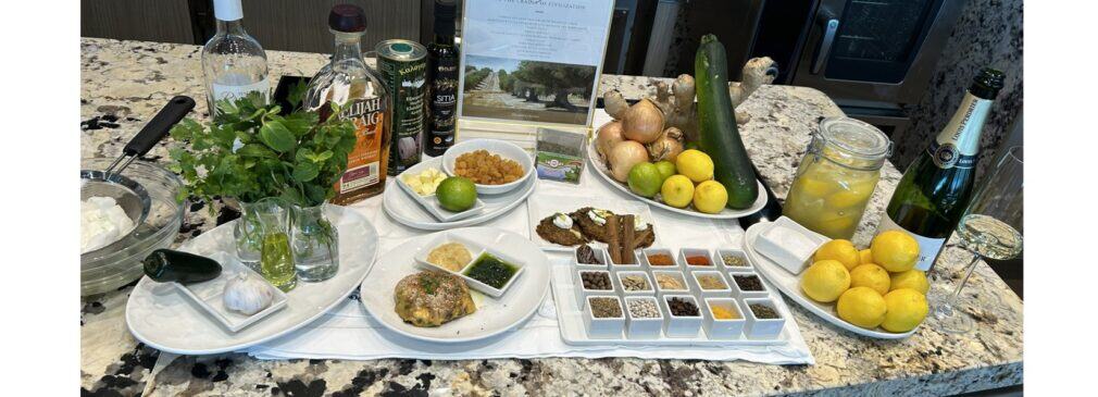 Cooking station with fresh vegetables, citrus, spices, olive oil, and cooking ingredients arranged on granite counter.
