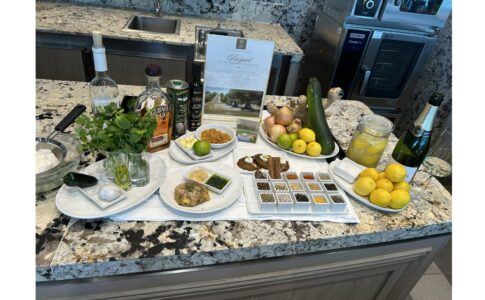 Cooking station with fresh vegetables, citrus, spices, olive oil, and cooking ingredients arranged on granite counter.