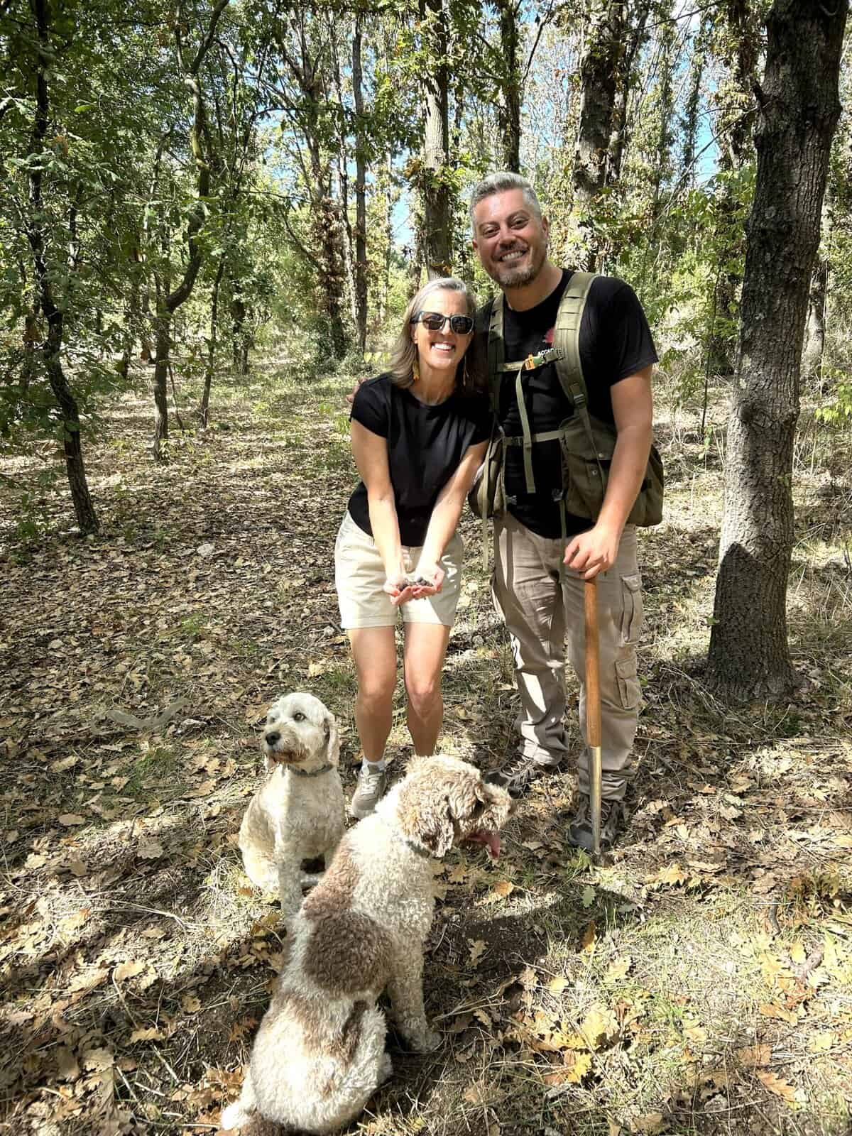 Author and truffle hunter with two truffle dogs in forest, woman holding freshly found truffles.