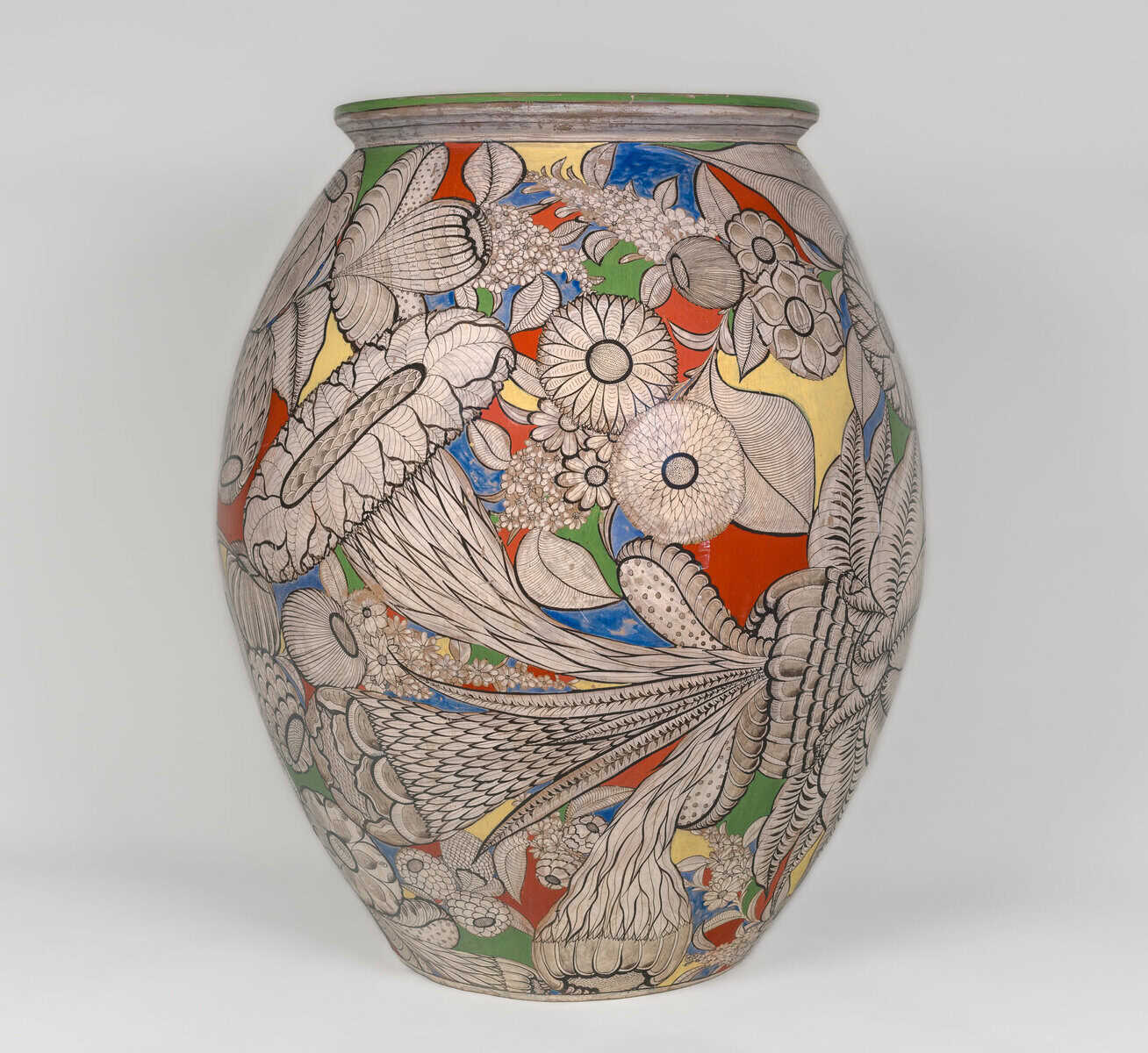 Large, rounded ceramic jar covered in dense floral and botanical designs outlined in black, with fields of bright color—red, blue, yellow, and green—filling the spaces between leaves, petals, and seed pods; the rim is edged in green against a light gray background.