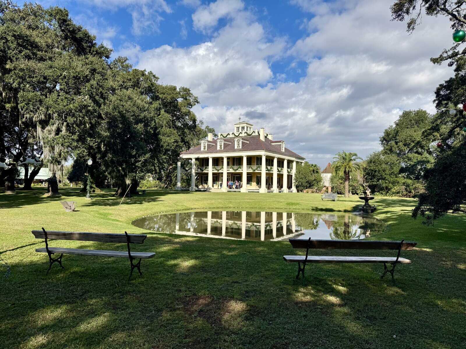A Greek revival-style mansion with columns, its image reflected in a small pond.