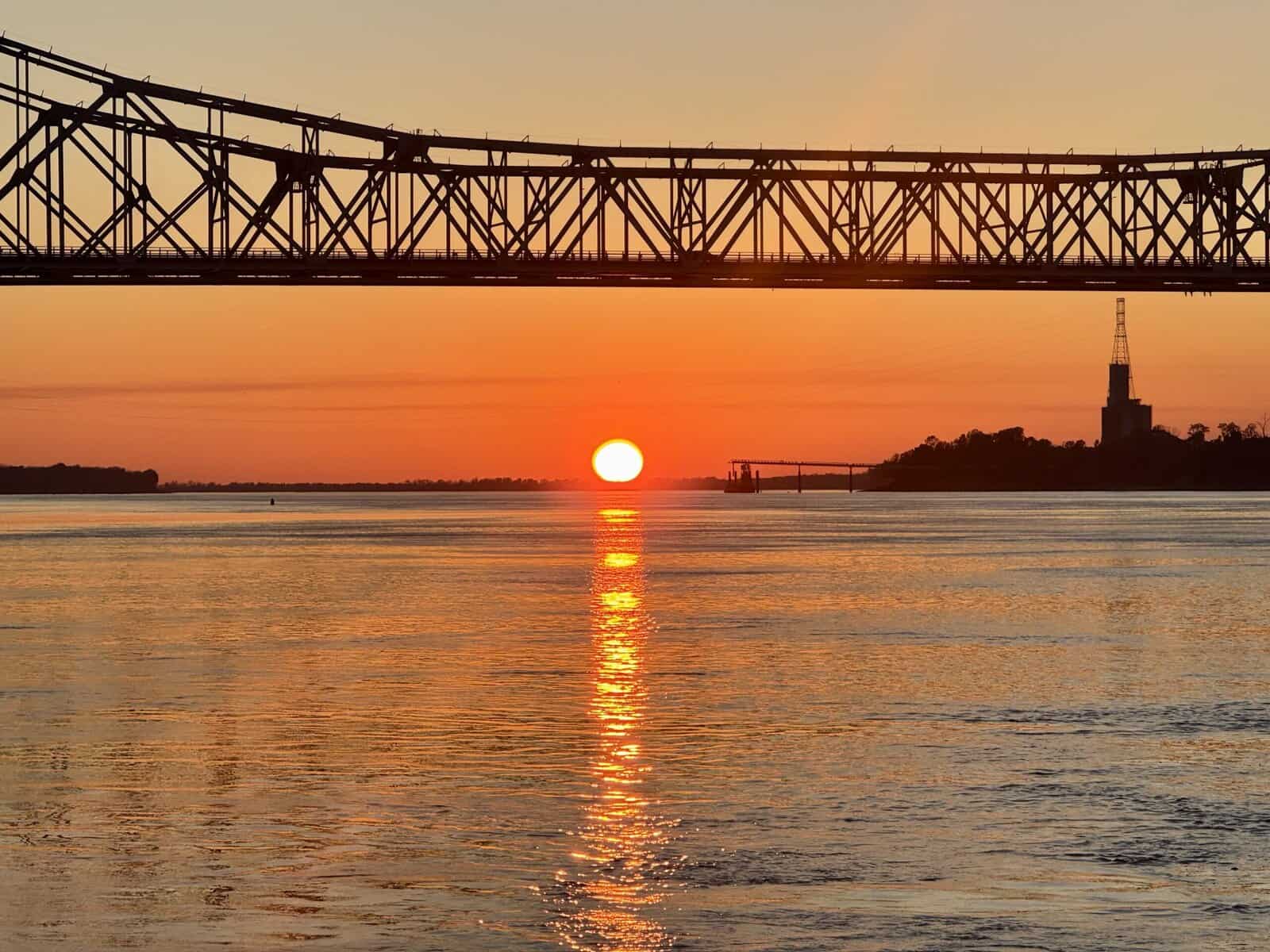 Setting sun under a bridge is reflected in the river.
