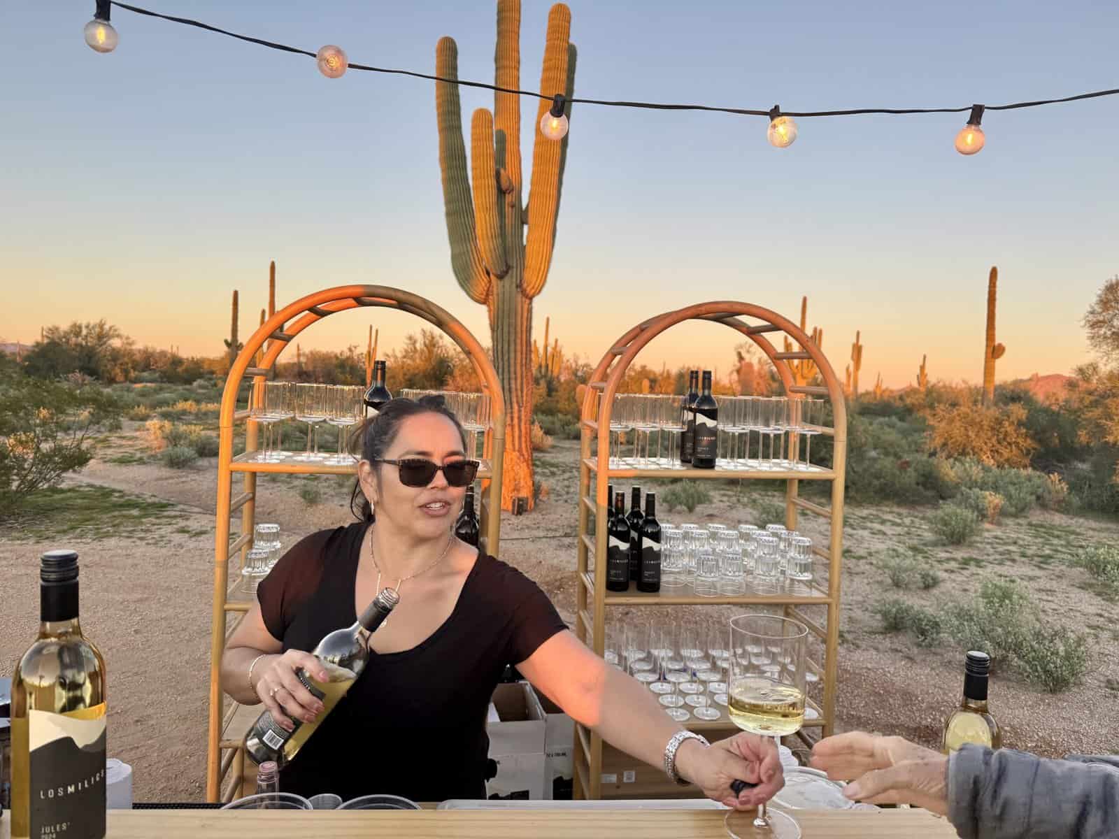 A woman serves wine in the desert.