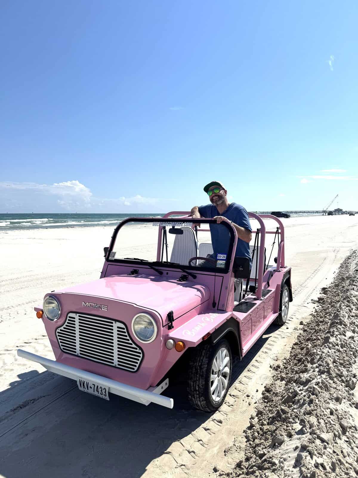 A driver poses with his pink Moke buggy parked in the sand.