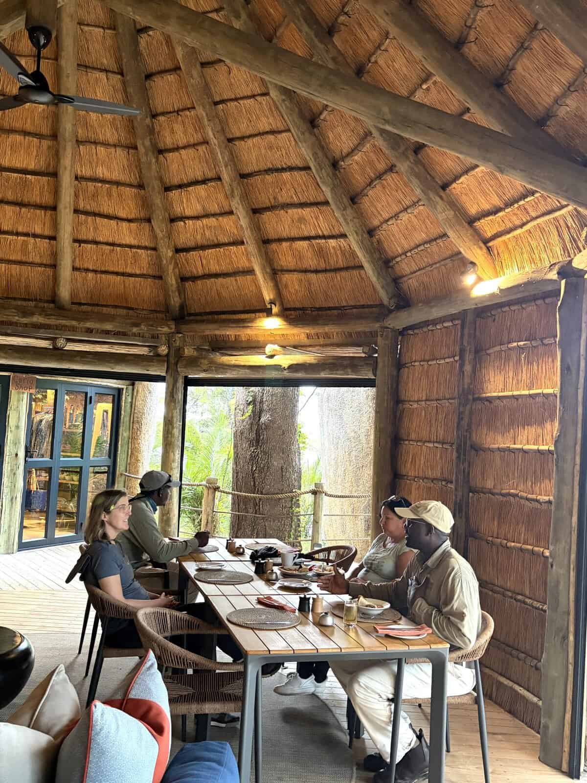 Lodge interior with thatched roof and guests dining at wooden table.