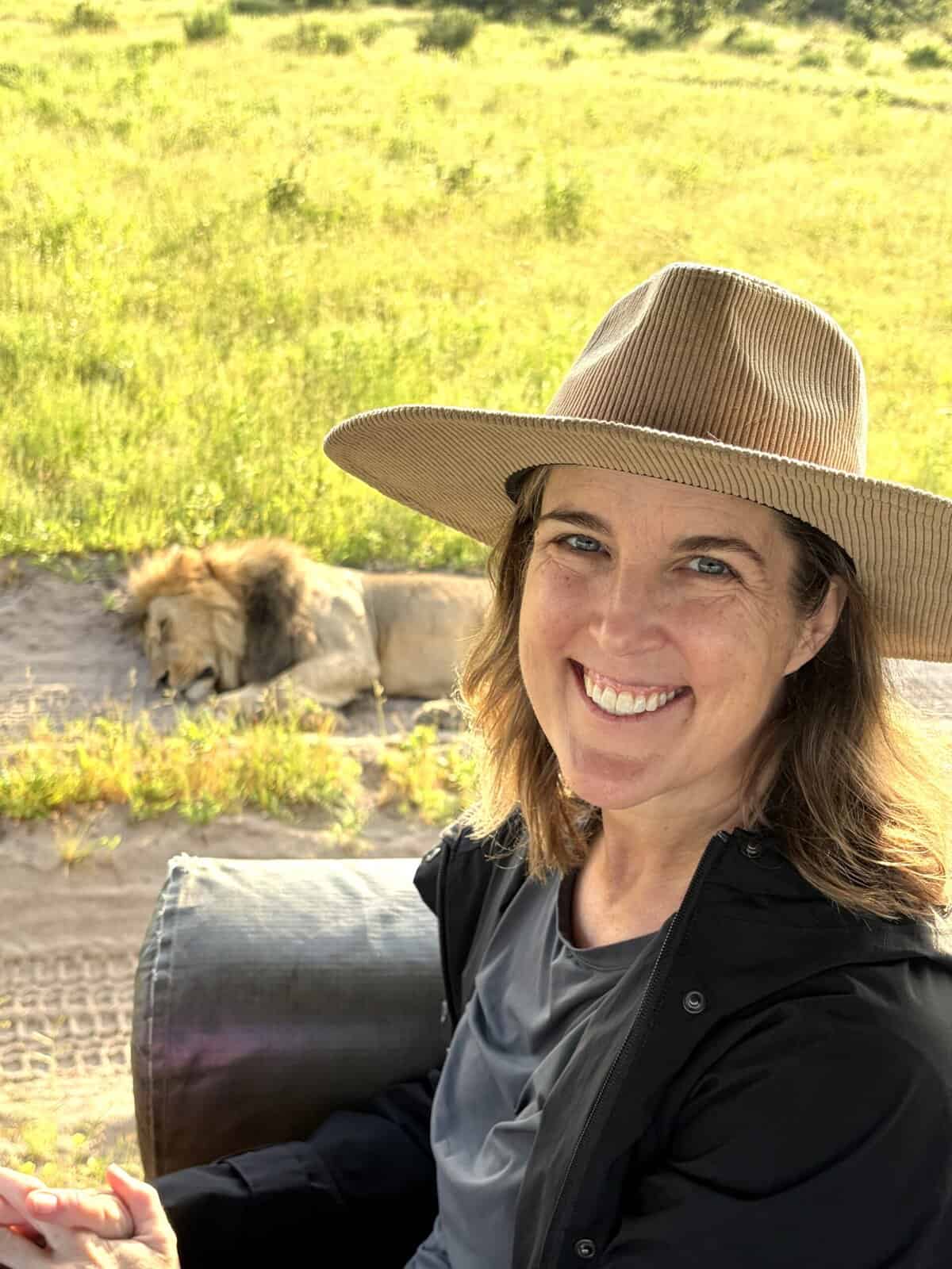 Woman in safari hat smiling with lions resting in background in Botswana.