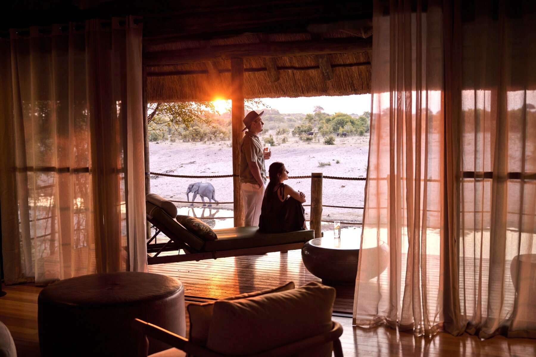 Lodge room interior with couple on viewing deck watching elephants at sunset.