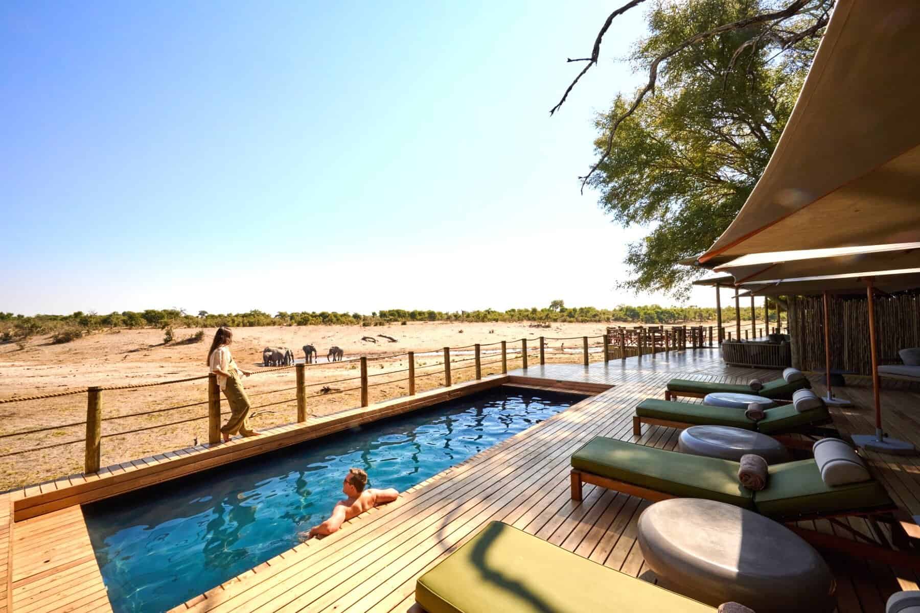 Swimming pool on wooden deck with elephants at waterhole in background at Savute Safari Lodge.