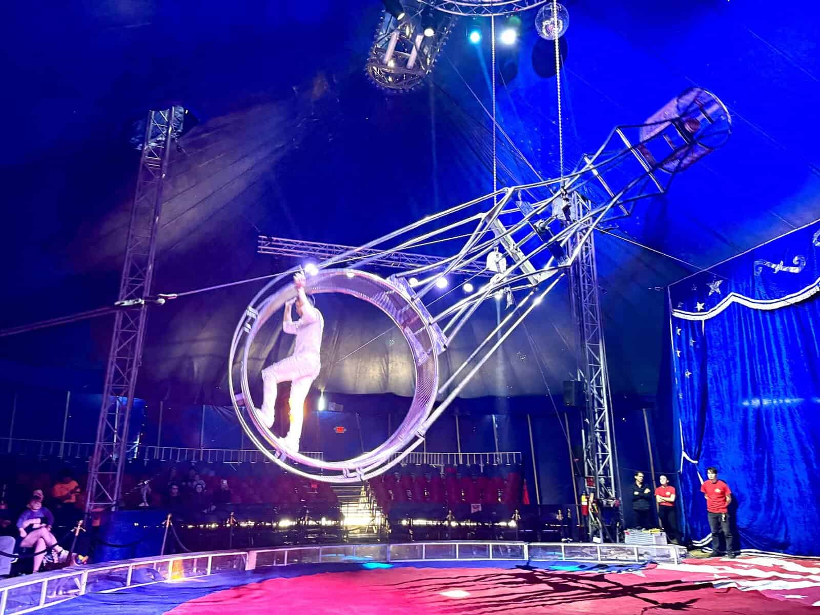 Man dressed in all white runs inside a large wheel, suspended in the air.