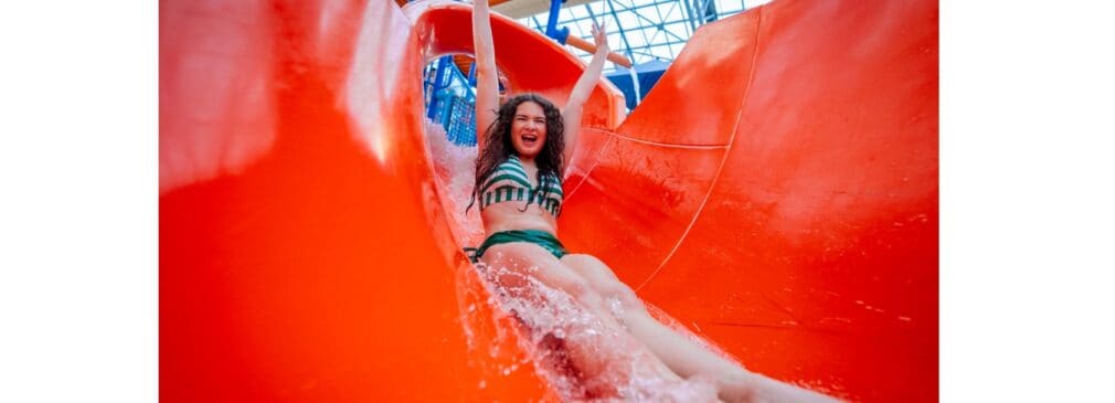 Girl in green and white striped bikini bathing suit goes down red waterslide.