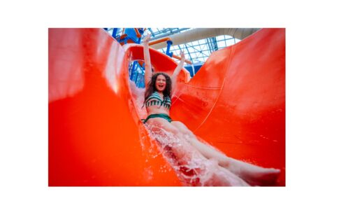 Girl in green and white striped bikini bathing suit goes down red waterslide.