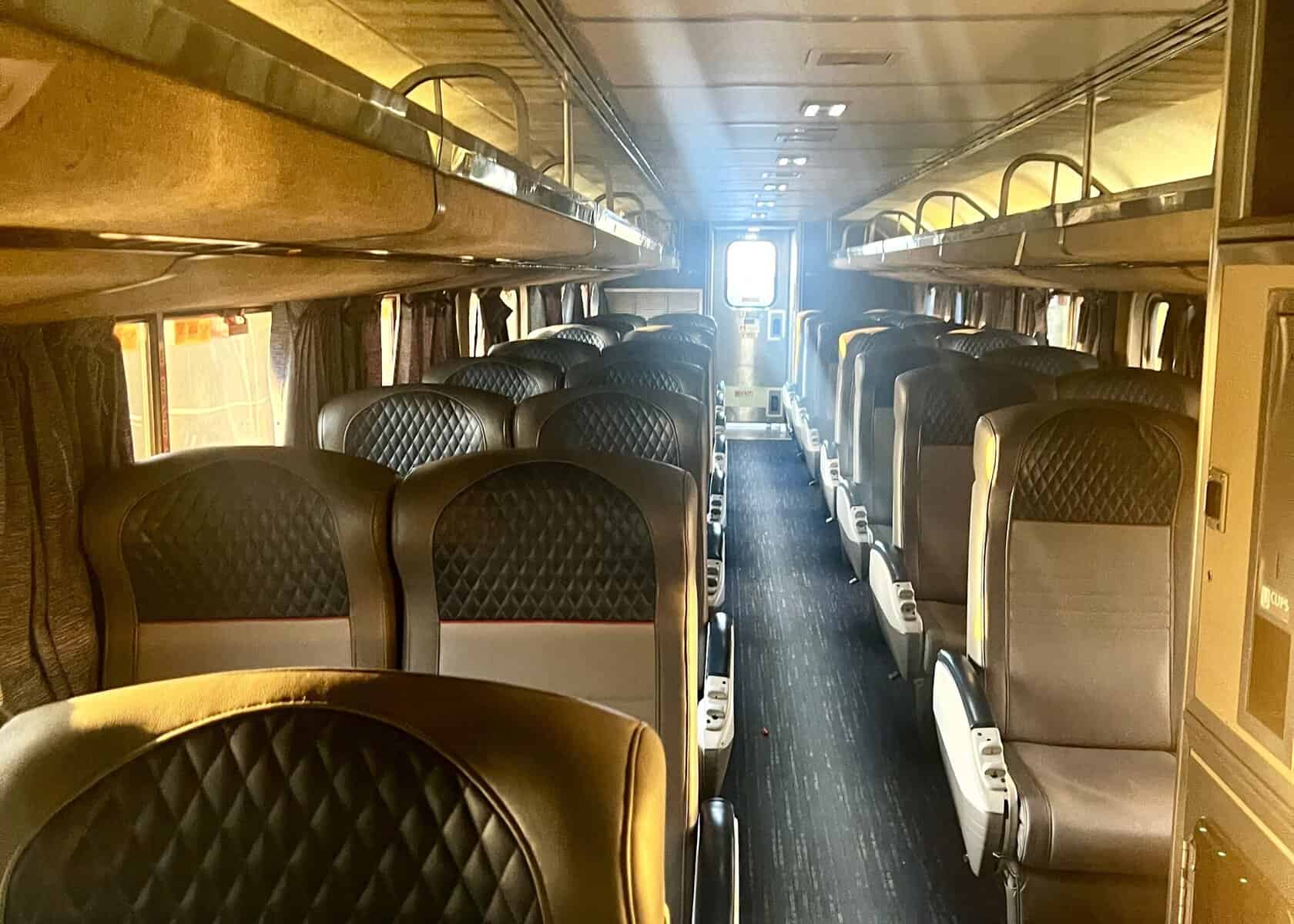 pairs of chairs separated by an aisle on the lower deck of a train.