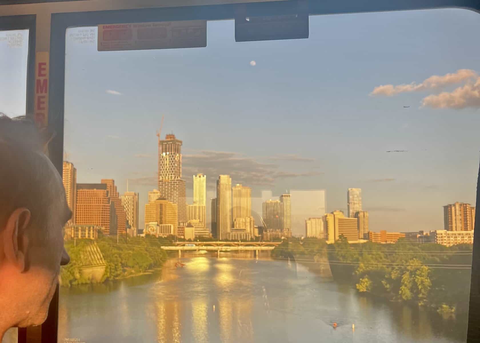 man looks out train window at Austin skyline behind the lake