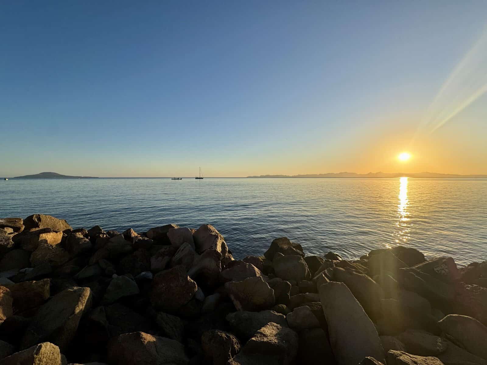 Rocks in the foreground; sunrise over mountains and the sea in the background