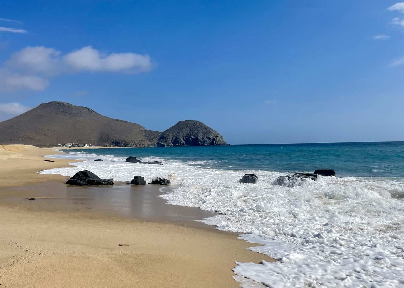Turquoise ocean meets the beach with mountains in the background