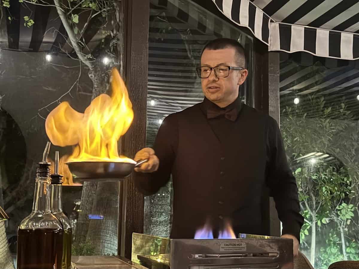Server tableside at Melvyn’s Restaurant flambes a steak in a pan, creating a dramatic flame. 