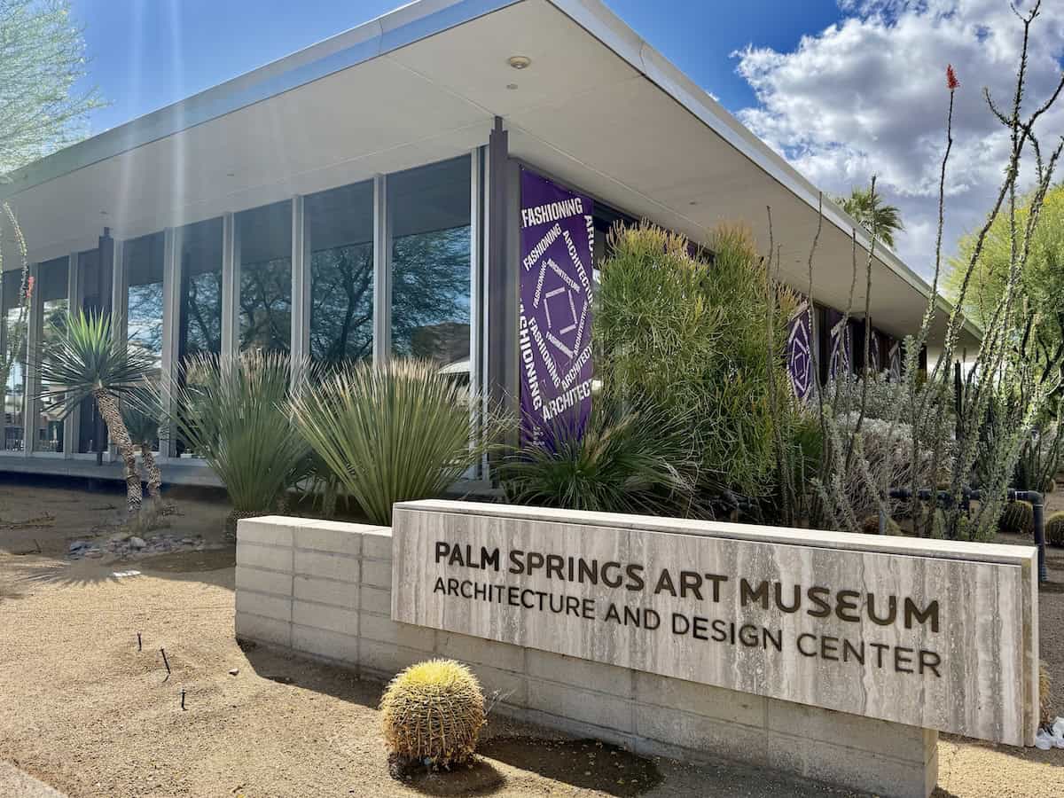 Exterior of the Palm Springs Art Museum Architecture and Design Center with marble signage and purple banners. 