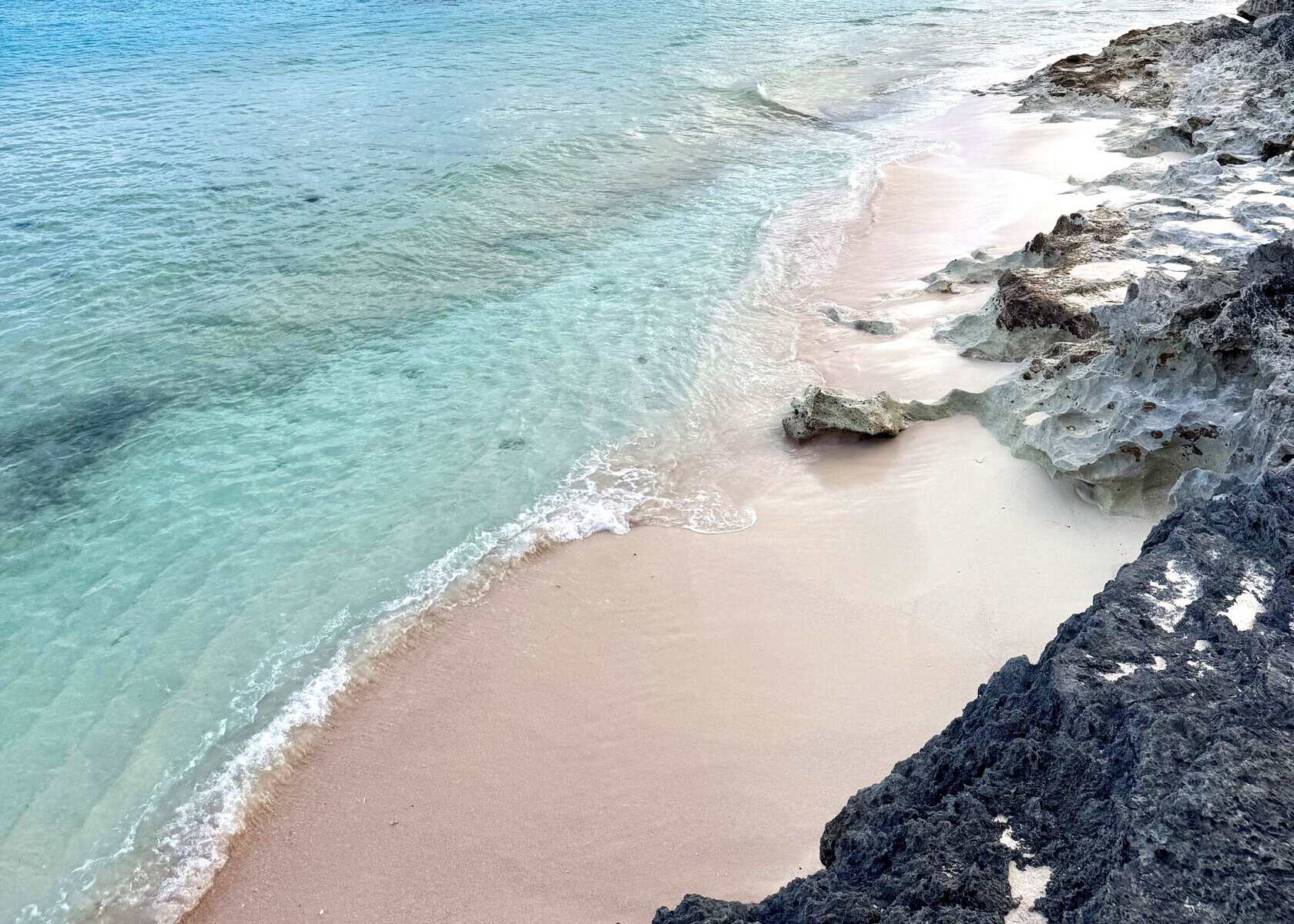 ocean waves on a rocky shore with pink sand beach