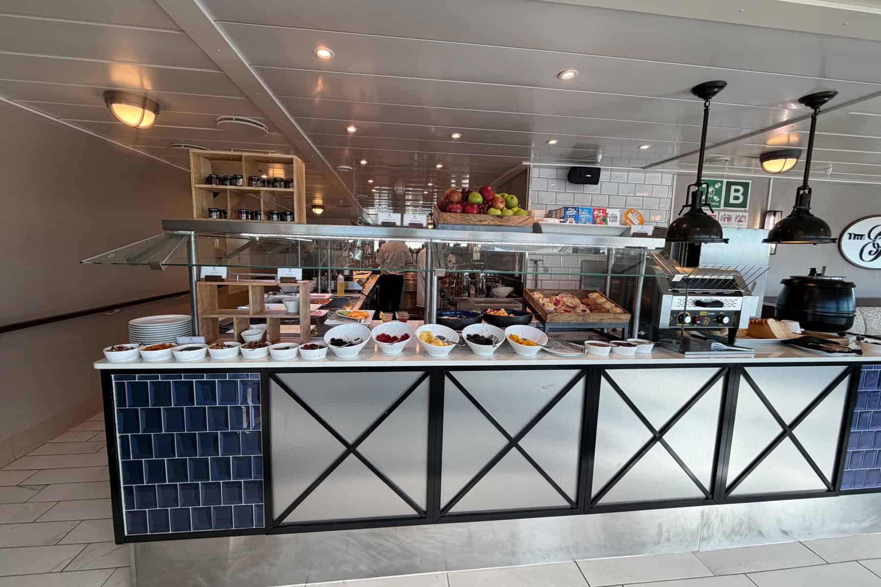  A buffet counter set with bowls of fruit, pastries, and cereal.
