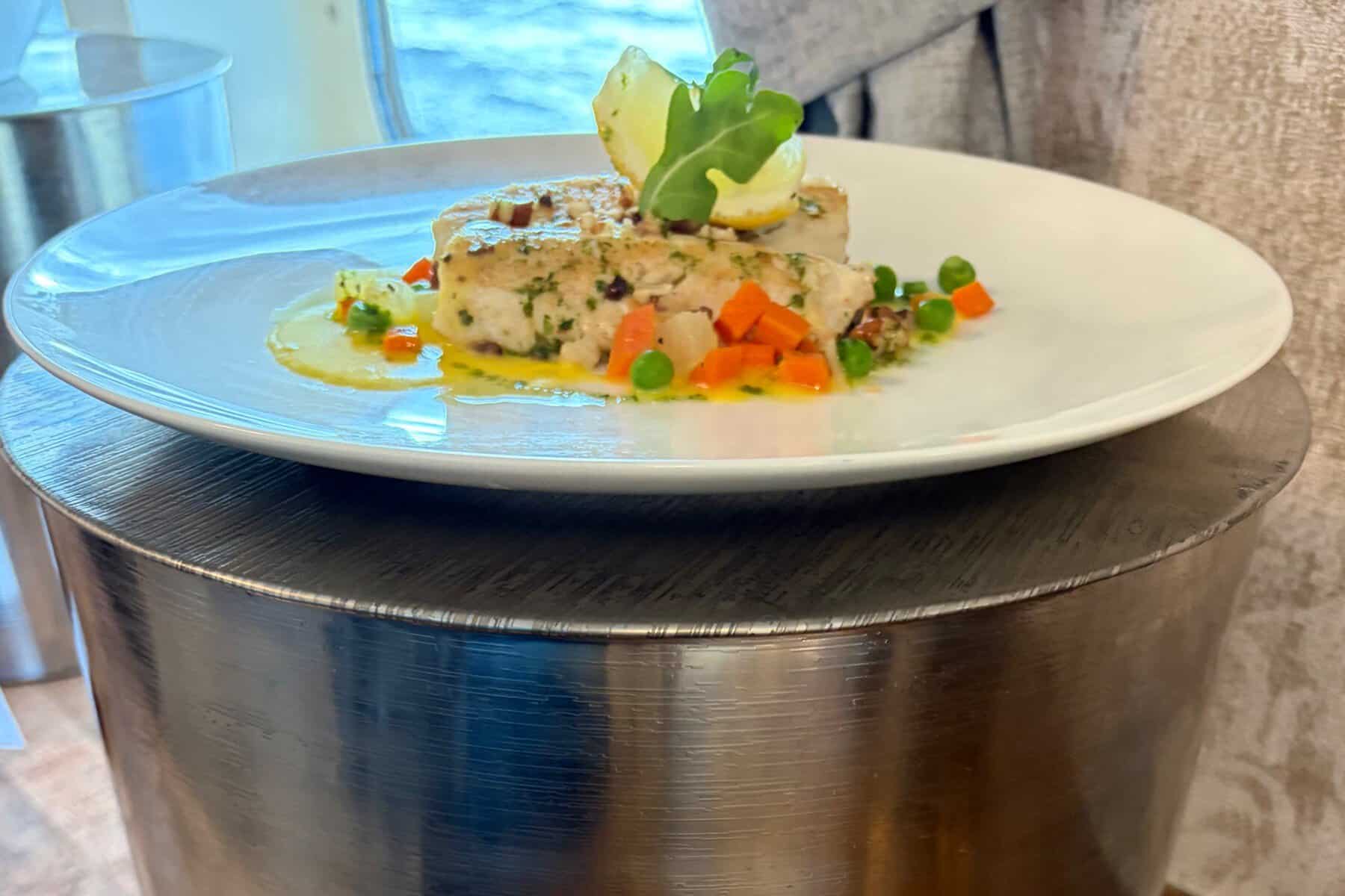  A white fish fillet with diced vegetables on a white plate.