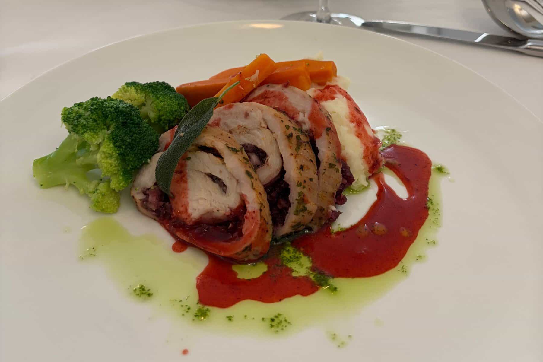 A plated turkey roulade with broccoli and carrots on a white plate.